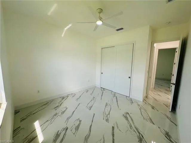Unfurnished bedroom featuring light marble finish floors, ceiling fan, and a closet