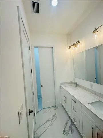 Bathroom featuring double vanity and light marble finish floors