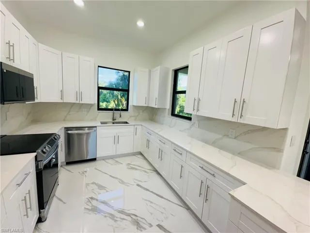 Kitchen featuring stainless steel appliances, decorative backsplash, light stone countertops, white cabinetry, and recessed lighting