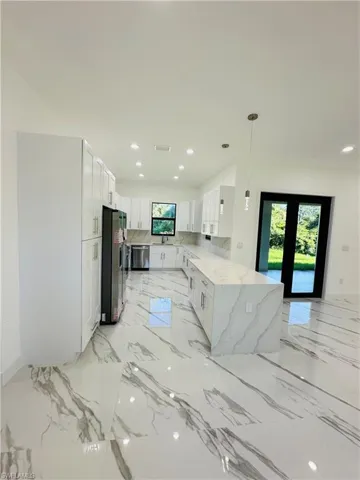 Kitchen featuring light stone countertops, white cabinetry, light marble finish flooring, recessed lighting, and hanging light fixtures