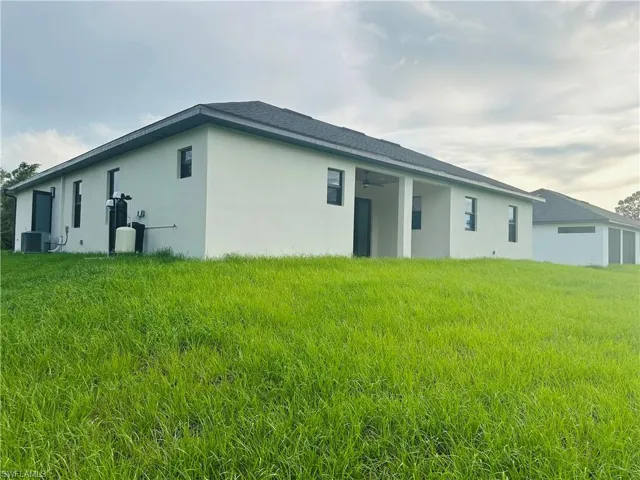 Rear view of house with stucco siding, a yard, ceiling fan, and roof with shingles