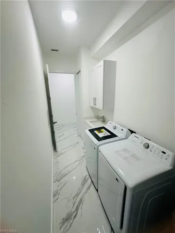 Laundry room featuring light marble finish floors, cabinet space, and washing machine and clothes dryer