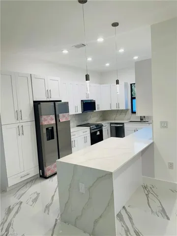 Kitchen featuring light marble finish flooring, a peninsula, light stone countertops, black appliances, and white cabinetry