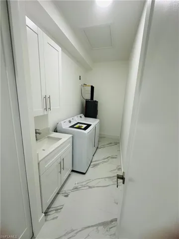 Laundry area featuring cabinet space, light marble finish floors, washing machine and clothes dryer, and attic access