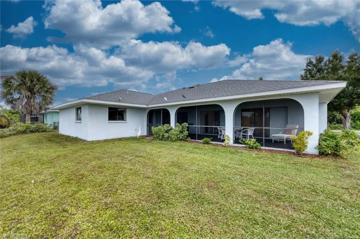 Back of property with stucco siding, a lawn, and a sunroom