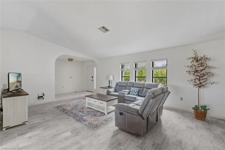 Living area featuring arched walkways, wood tiled floors, and vaulted ceiling