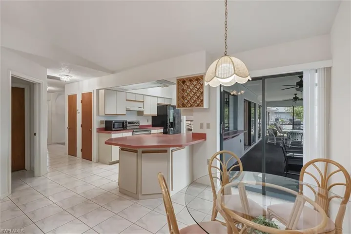 Kitchen featuring stainless steel appliances, a peninsula, hanging light fixtures, light tile patterned floors, and white cabinetry