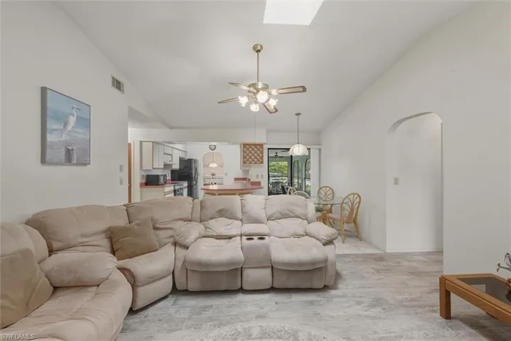 Living room with vaulted ceiling, ceiling fan, arched walkways, and a skylight