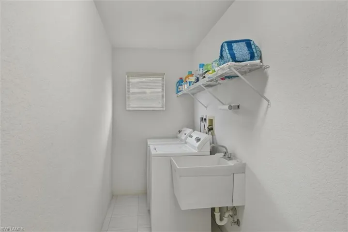 Washroom with tile patterned floors, a textured wall, and independent washer and dryer
