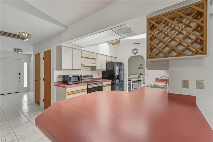 Kitchen featuring arched walkways, appliances with stainless steel finishes, light countertops, a peninsula, and white cabinetry