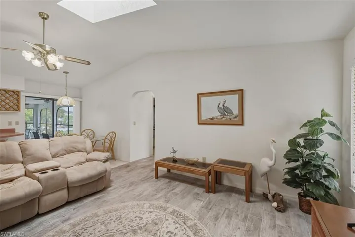 Living room with lofted ceiling, light wood-style floors, a skylight, arched walkways, and a ceiling fan