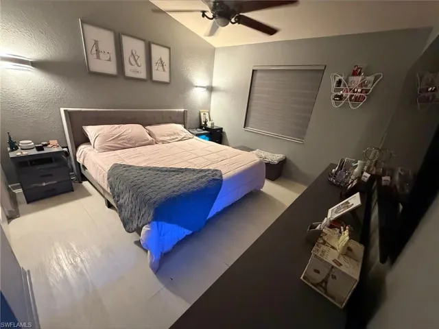 Bedroom featuring light-toned wood-finish flooring, textured walls, and a ceiling fan with integrated lighting