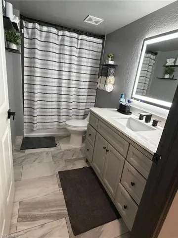 Bathroom featuring a gray vanity with a single sink, an illuminated mirror, and large format floor tiling
