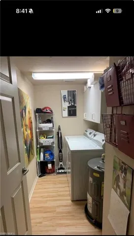 Dedicated laundry area featuring wood-finish flooring, white overhead cabinetry, and a fluorescent ceiling light fixture