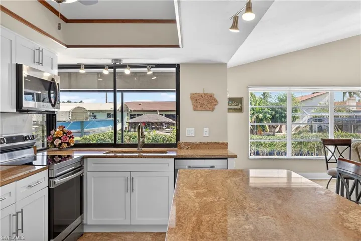 Kitchen with stainless steel appliances, track lighting, white cabinets, and light stone countertops