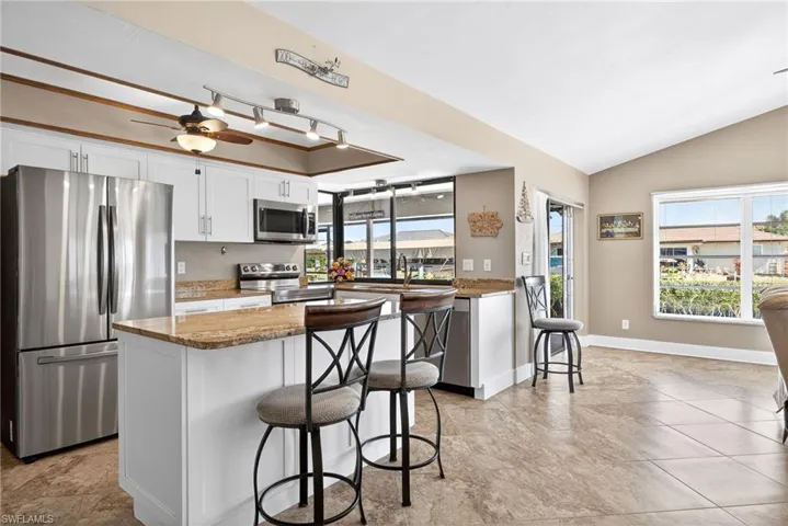 Kitchen featuring appliances with stainless steel finishes, a kitchen breakfast bar, white cabinets, dark stone countertops, and lofted ceiling