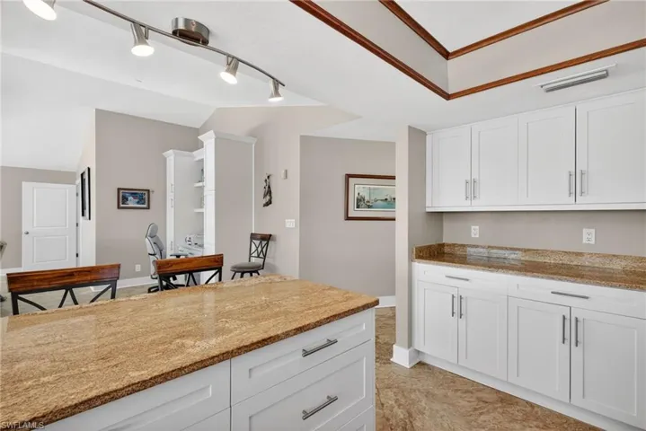 Kitchen featuring white cabinets, light stone counters, lofted ceiling, and rail lighting