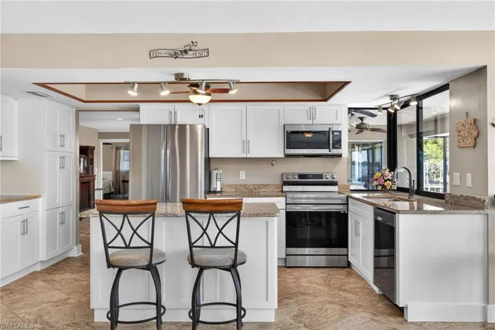 Kitchen featuring stainless steel appliances, white cabinetry, light stone countertops, a kitchen bar, and a center island