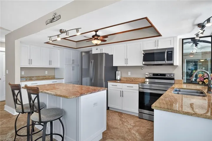 Kitchen featuring stainless steel appliances, white cabinetry, a ceiling fan, a breakfast bar, and light stone counters