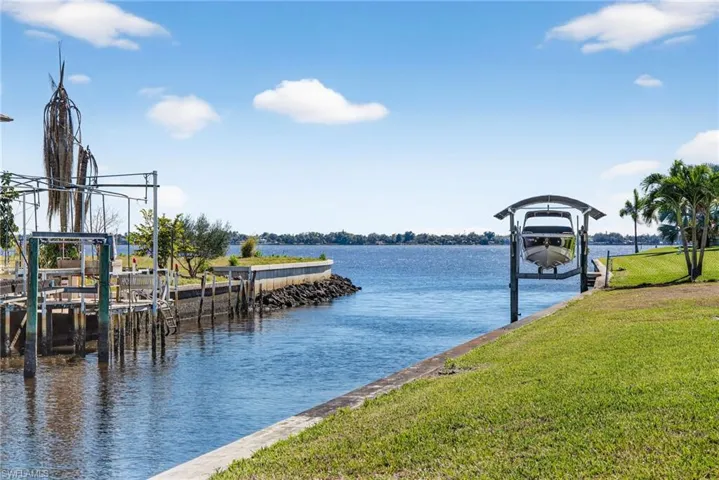 Dock area with boat lift, a water view, and a yard