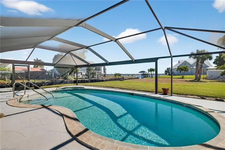 View of swimming pool featuring a lawn, glass enclosure, a sunroom, a pool with connected hot tub, and a patio area