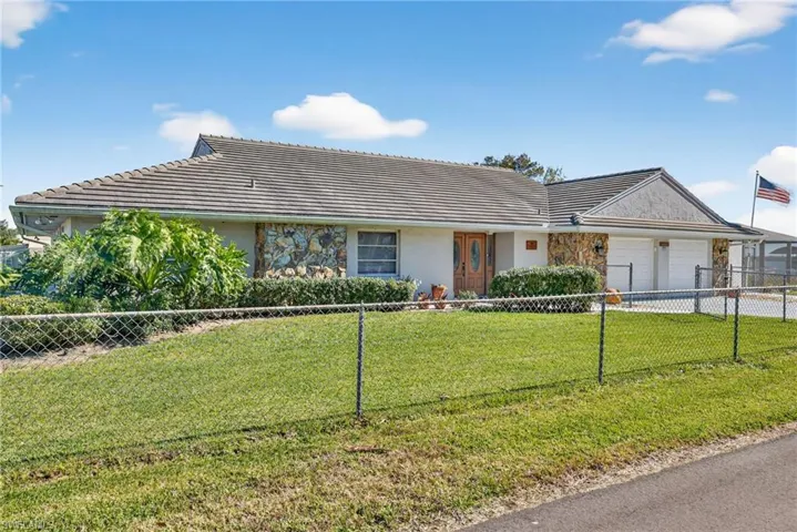Ranch-style home with a fenced front yard, stucco siding, a garage, a tiled roof, and stone siding