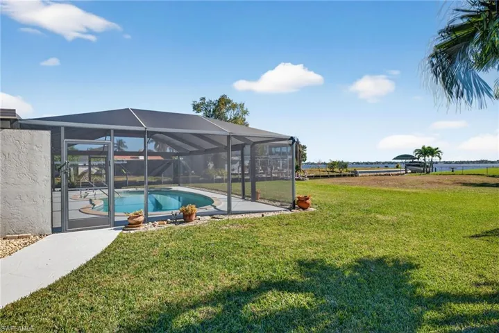 View of grassy yard with an outdoor pool, glass enclosure, a sunroom, a patio area, and a water view