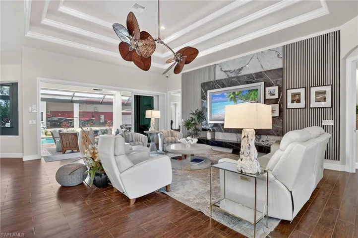 Living area featuring a tray ceiling, wood floors, decorative crown molding, arched walkways, and a ceiling fan and a new 85" Samsung Art TV with a custom marble feature wall