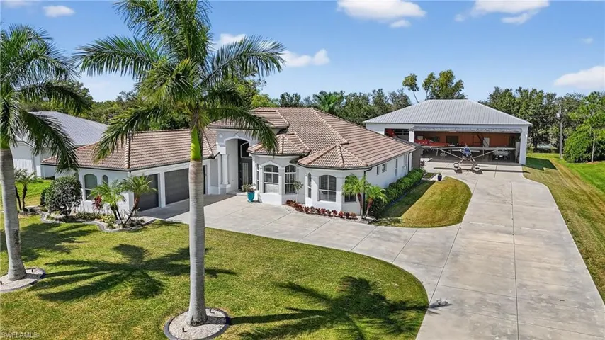Rear view of property with a yard, a tiled roof, driveway, and stucco siding