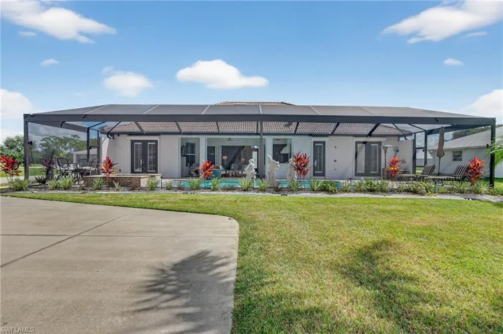 View of back of home featuring glass enclosure, a back lawn