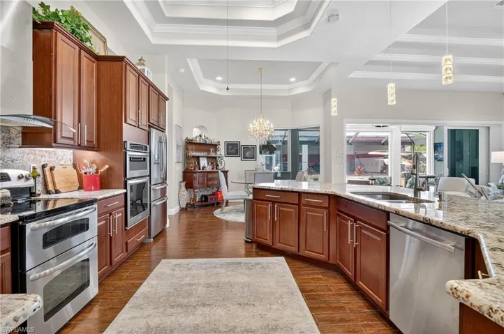 Kitchen with a tray ceiling, stainless steel appliances, new lighting, stone counters, decorative light fixtures, and crown molding