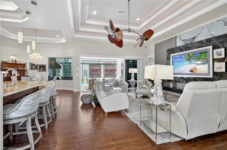 Living and breakfast bar area featuring a tray ceiling, wood-style tile flooring, decorative crown molding, arched walkways, and a ceiling fan and a new 85" Samsung Art TV with a custom marble feature wall