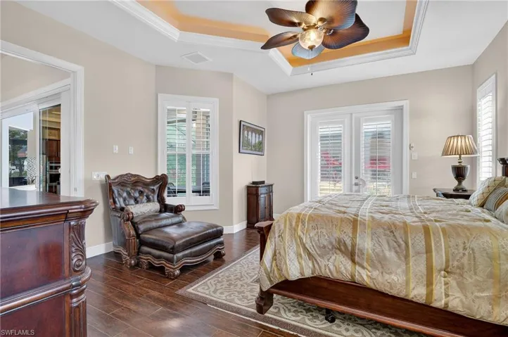 Bedroom with a tray ceiling, dark wood-style tile flooring, ceiling fan, ornamental molding, and access to pool and lanai