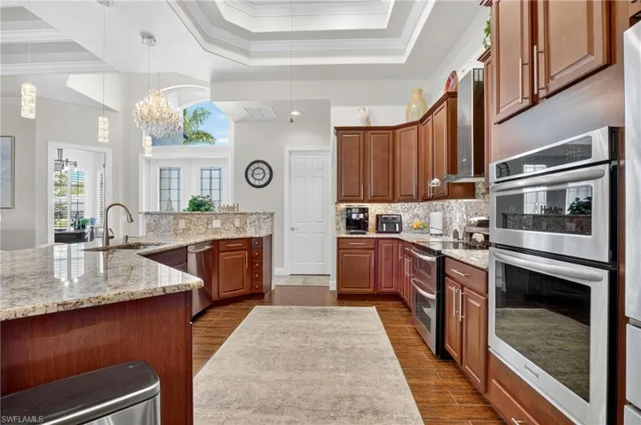 Kitchen with stainless steel appliances, new decorative light fixtures, crown molding, light stone countertops, and dark wood-style tile flooring