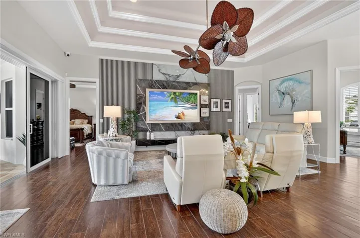 Living area featuring a tray ceiling, wood-style tile flooring, crown molding, arched walkways, and a ceiling fan anda new 85" Samsung Art TV with a custom marble feature wall