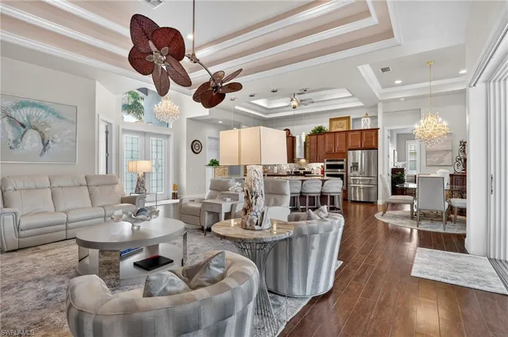 Living area with a chandelier, a raised ceiling, dark wood-style tile flooring, ornamental molding, and a ceiling fan
