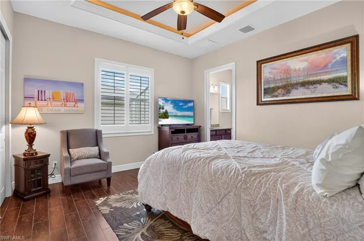 Bedroom with a tray ceiling, dark wood-style tile flooring, ensuite bath, and ceiling fan