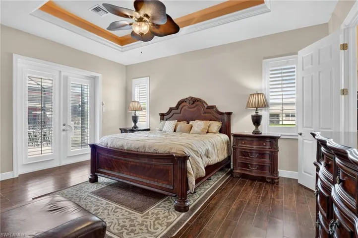 Bedroom with a raised ceiling, dark wood-style tile flooring, ceiling fan, and access to exterior