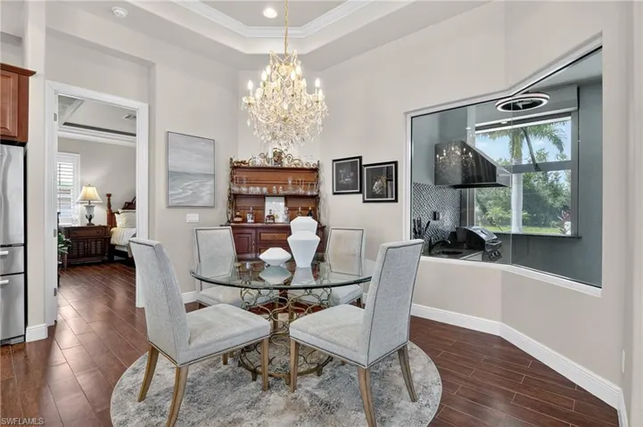 Dining room featuring a chandelier, dark wood-style tile flooring, ornamental molding, a raised ceiling, and recessed lighting