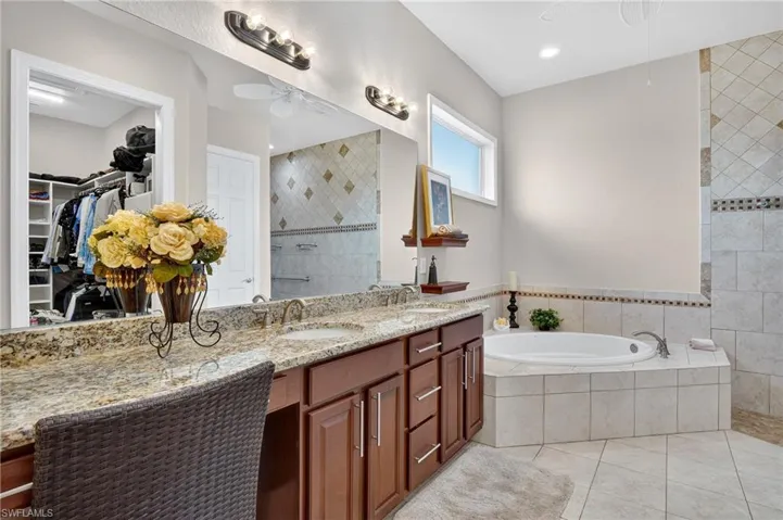 Full bathroom with a walk in closet, double vanity, light tile patterned floors, a garden tub, and ceiling fan
