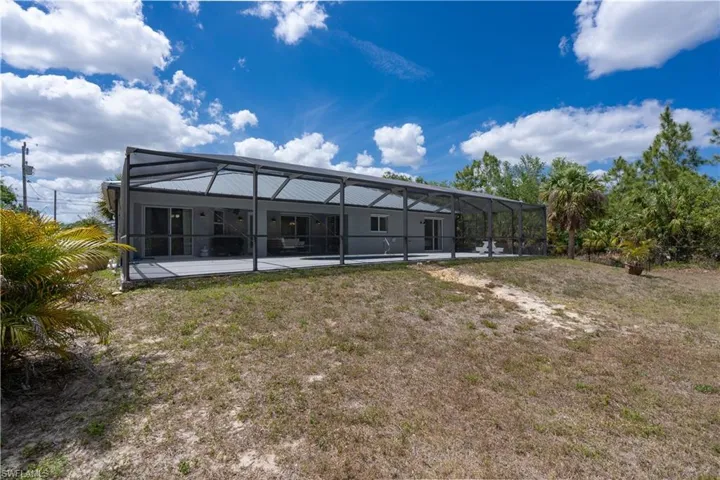 Back of property featuring a lawn, glass enclosure, an outdoor pool, and a patio