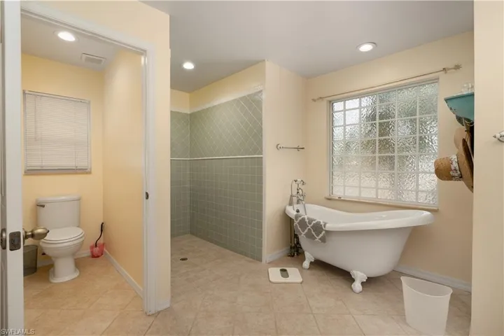Bathroom featuring a tile shower, a soaking tub, toilet, and baseboards