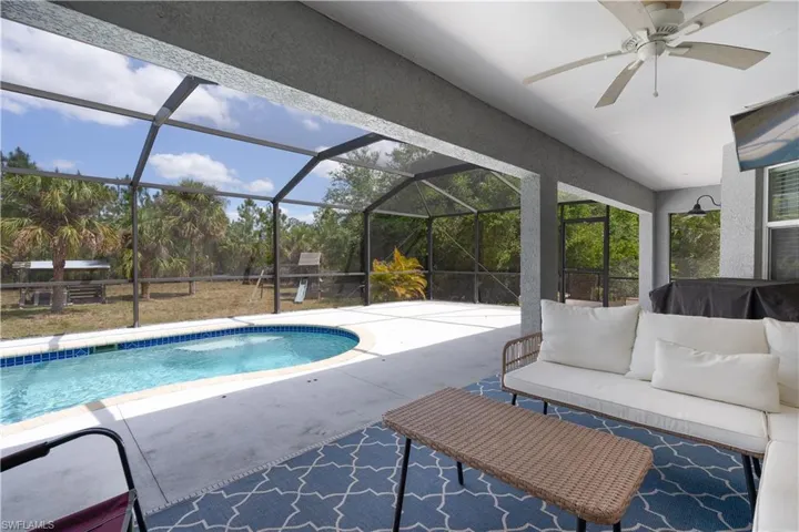 Outdoor pool with an outdoor hangout area, a ceiling fan, glass enclosure, and a patio