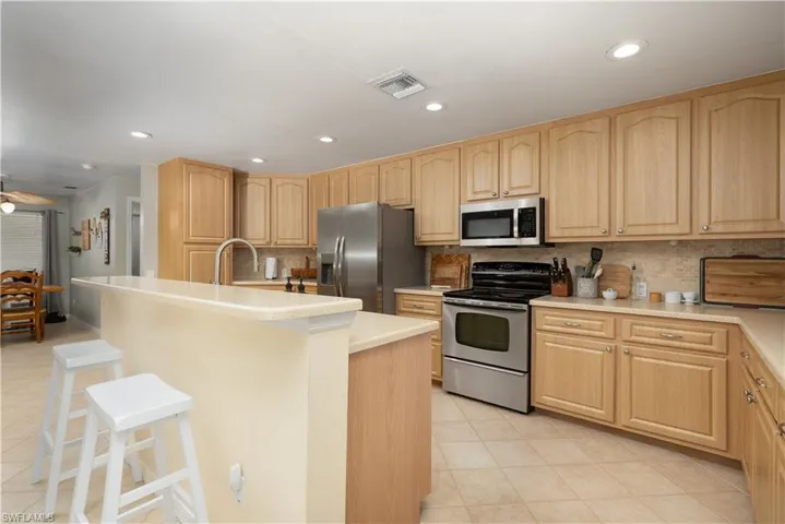 Kitchen with visible vents, a kitchen bar, backsplash, light brown cabinets, and appliances with stainless steel finishes