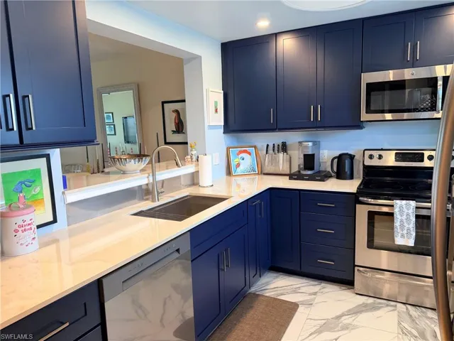 Kitchen featuring blue cabinetry, stainless steel appliances, white countertops, and marble-look flooring