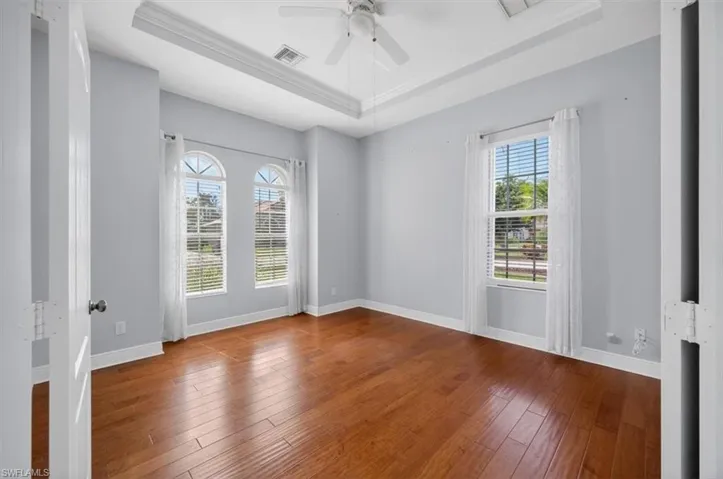 Empty room with a raised ceiling, hardwood / wood-style floors, ceiling fan, and crown molding