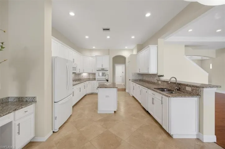 Kitchen cabinetry, white appliances, arched walkways, and recessed lighting