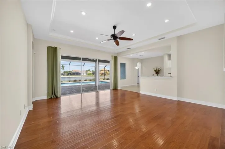 Unfurnished living room with ceiling fan, a tray ceiling, hardwood / wood-style flooring, and recessed lighting