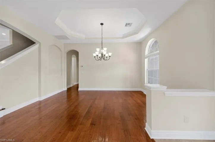Unfurnished dining area featuring dark wood-style floors, arched walkways, suspended lighting, ornamental molding, and a raised ceiling