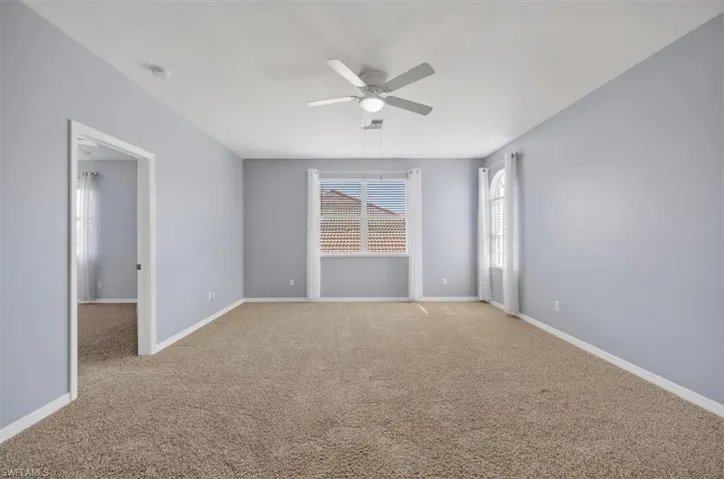 Carpeted spare room featuring ceiling fan and baseboards